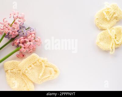Rosafarbene und lila Hyazinthen-Blumen, gelbe Stiefel und Handschuhe für ein Neugeborenes auf weißem Hintergrund mit Kopierbereich. Muttertag Grußkarte. Schreib Weisheit Stockfoto