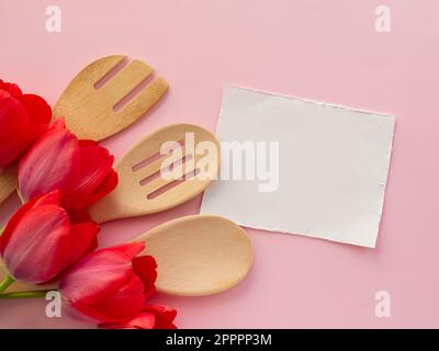 Rote Tulpen mit Küchenutensilien auf pinkfarbenem Hintergrund mit weißem Papier und Kopierbereich. Grußkarte zum Frauen- und Muttertag. Glückwunsch zum Geburtstag Stockfoto