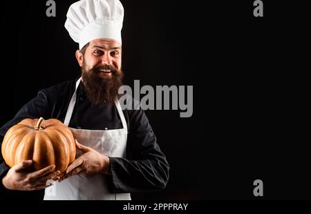 Koch in Uniform mit Kürbis. Ein bärtiger Mann mit Kochmütze und Kürbis. Bio-Lebensmittel. Koch Koch in weißer Schürze mit Kürbis für kulinarische Gerichte. Thanksgiving-Tag Stockfoto