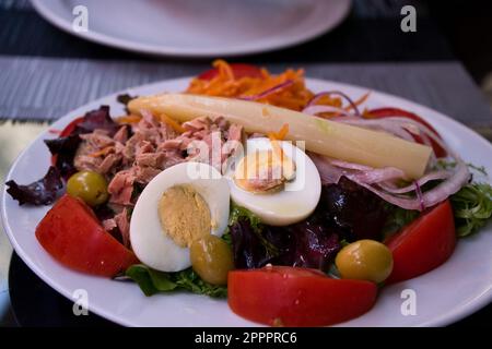 Köstlicher frischer Salat mit Thunfisch und Gemüse, Salat, Tomaten, Oliven, Karotten und Spargel auf einem Tisch. Gesunde mediterrane Ernährung. Stockfoto