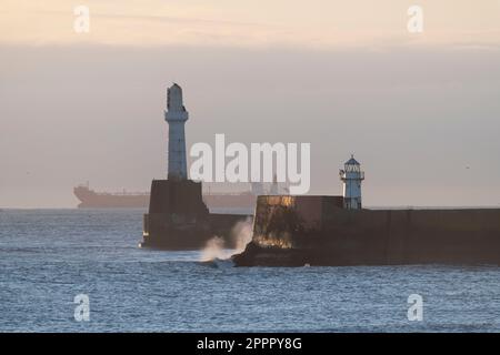 South Breakwater Lighthouse & North Pier Light am Eingang zum Hafen von Aberdeen bei Sonnenschein am frühen Morgen mit einem Öltanker am Horizon Stockfoto