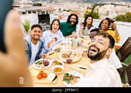 Fröhliche junge Gruppe multiethnischer Freunde, die ein Barbecue-Dinner auf dem Dach genießen Stockfoto