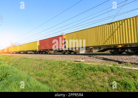 Güterzug, der Container transportiert, die an einem sonnigen Frühlingstag in Bewegung sind. Bewegungsunschärfe. Stockfoto