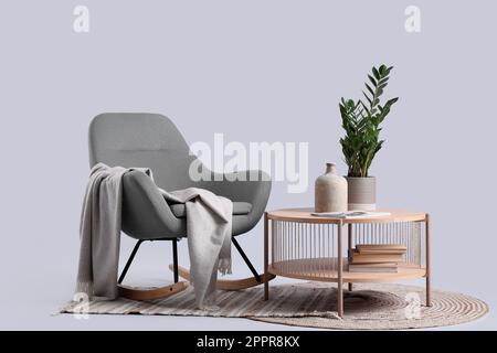 Hölzerner Kaffeetisch mit Zimmerpflanzen und Vase neben dem gemütlichen Schaukelstuhl auf grauem Hintergrund Stockfoto