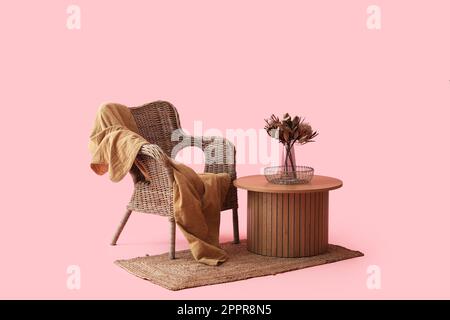 Couchtisch mit getrockneten Blumen in Vase neben einem gemütlichen Sessel auf pinkfarbenem Hintergrund Stockfoto