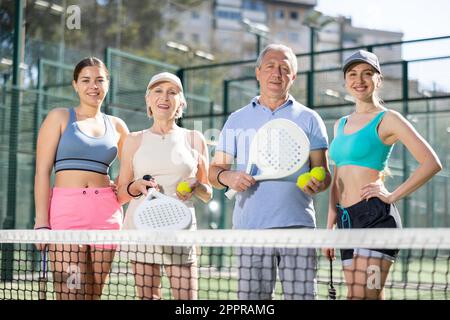 Eine Gruppe von Tennisspielern, die sich neben dem Netz postieren und Padel-Schläger halten Stockfoto