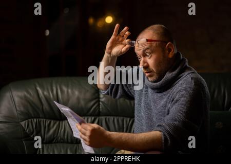 Ein Mann ist schockiert von einem Brief aus Papier. Schlechte Nachrichten führen zu Stress. Steuererhöhung, schlechte Kommunikation. Schwarzweißbild. Stockfoto