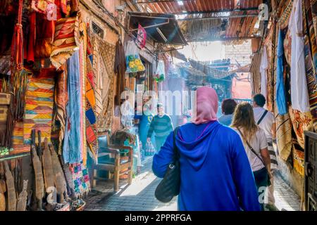 Marrakesch, Marokko - 19. Oktober 2015. Am frühen Morgen im Old City Souk, während Fußgänger auf einer schmalen Straße an Geschäften vorbeigehen, die touristische Waren verkaufen. Stockfoto