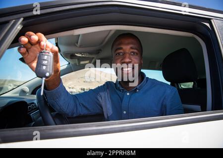 Ein glücklicher Afrikaner hält seine Autoschlüssel, während er auf dem Fahrersitz sitzt. Stockfoto