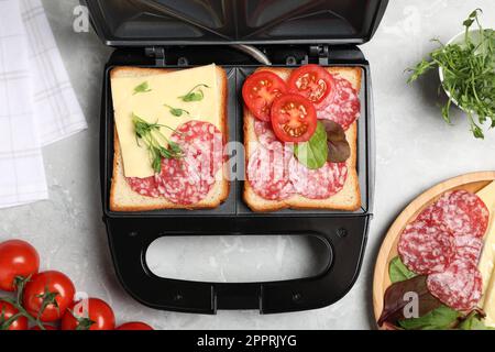 Moderne Grillmaschine mit Sandwiches und verschiedenen Produkten auf hellgrauem Tisch, flach liegend Stockfoto