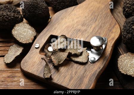 Rasierer mit ganzen und geschnittenen schwarzen Trüffeln auf Holztisch, Nahaufnahme Stockfoto