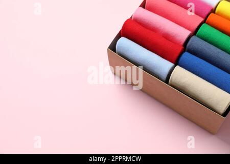 Box mit verschiedenen bunten Socken auf hellrosa Hintergrund. Platz für Text Stockfoto