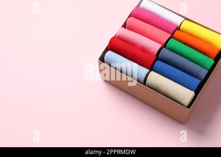 Box mit verschiedenen bunten Socken auf hellrosa Hintergrund. Platz für Text Stockfoto