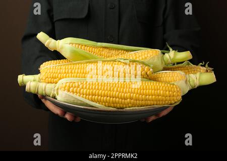 Eine Frau mit leckeren frischen Maiskolben auf braunem Hintergrund, Nahaufnahme Stockfoto