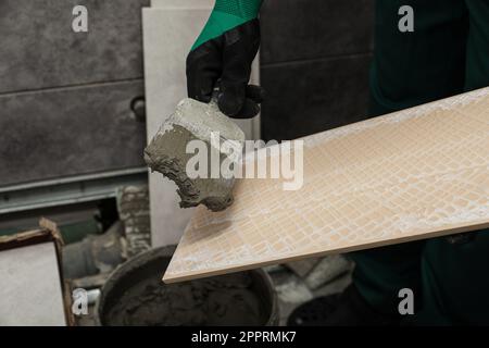 Arbeiter, der Klebstoffmischung auf Keramikfliesen mit Spachtel aufbringt, Nahaufnahme Stockfoto