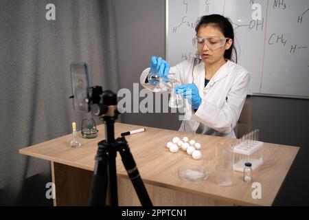 Online-Lehrer, Mentor. Klassenzimmer für Schulwissenschaften. Der Lehrer erklärt Chemie. Junge Frau unterrichtet und nimmt Videokurs auf, Smartphone auf einem Stativ Stockfoto