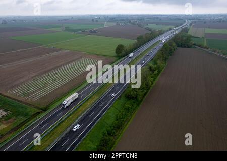 Piacenza, Italien - April 2023 Cargo LKWs und Pkw auf der Autobahn A1 Autostrada del Sone aus der Vogelperspektive zwischen padainflachen ländlichen Feldern Stockfoto