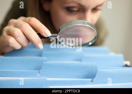 Eine Frau sieht sich Ordner in der Schublade durch eine Lupe an Stockfoto