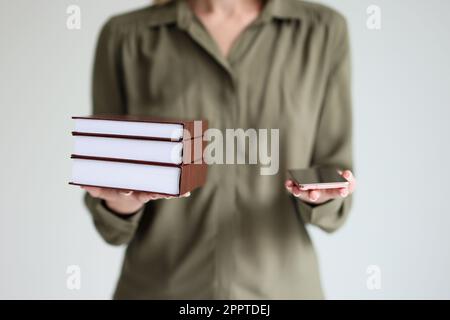 Frau hält ein modernes Mobiltelefon und einen Stapel Bücher in den Händen Stockfoto