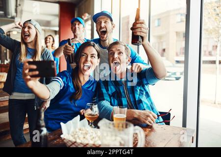 Die Erinnerungen an den Spieltag. Eine Gruppe von Freunden macht ein Selfie, während sie sich ein Sportspiel in einer Bar anschauen. Stockfoto