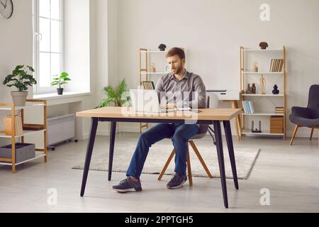 Ein Mann sitzt zu Hause an seinem Schreibtisch, verwendet ein Notebook, lernt online oder schreibt E-Mails Stockfoto