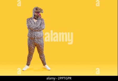 Komischer exzentrischer Übergewichtiger Mann, der sich in einer Dinosauriermaske auf dem Kopf und im Pyjama mit Leopardenmuster posiert Stockfoto