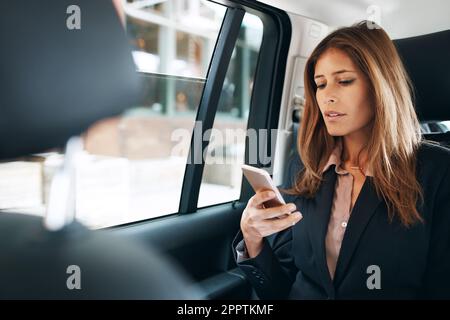 Verbindung auf dem Weg zur Arbeit. Eine reife Geschäftsfrau, die ein Handy auf dem Rücksitz eines Autos benutzt. Stockfoto