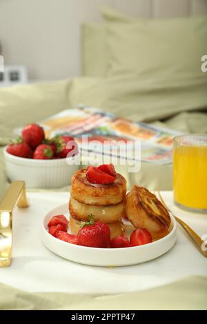 Leckeres Frühstück im Schlafzimmer. Hüttenkäse-Pfannkuchen mit Erdbeeren und Honig auf weißem Tablett Stockfoto