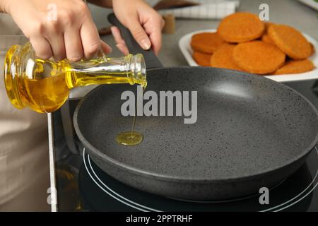 Eine Frau, die Öl in die Bratpfanne gießt, Nahaufnahme. Panierte Schnitzel kochen Stockfoto