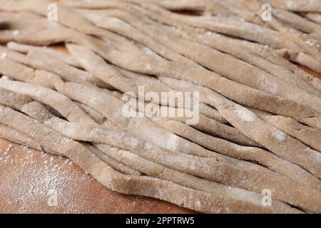 Ungekochtes hausgemachtes Soba (Buchweizennudeln) auf Holztisch, Nahaufnahme Stockfoto