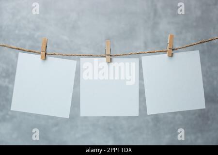 Holzkleidekabinen mit leeren Notizzetteln auf Garn vor grauem Hintergrund. Platz für Text Stockfoto