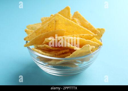 Tortilla-Chips (Nachos) in Glasschüssel auf hellblauem Hintergrund, Nahaufnahme Stockfoto