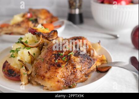 Gebackene Hähnchenschenkel mit Kartoffelpüree, gerösteten Zwiebeln und Äpfeln auf einem Teller Stockfoto