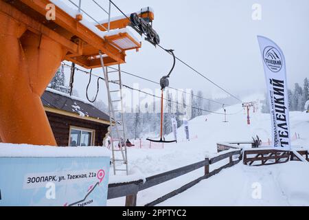 Iogach, Russland - 10. März 2018: Skigebiet Teletsky Altai. Klammerhebebühne auf dem Berg und Waldhintergrund bei Schneefall. Die Inschrift Stockfoto