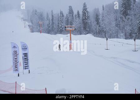 Iogach, Russland - 10. März 2018: Skigebiet Teletsky Altai in der Nähe von Iogach. Aufzug auf dem Berg und Waldhintergrund bei Schneefall. Der Eingang Stockfoto