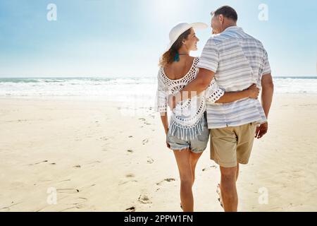 Ich bin froh, dass wir uns diesen Urlaub gönnten. Ein erwachsenes Paar, das am Strand spaziert. Stockfoto