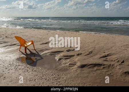 Plastikstuhl am sonnigen, nassen Sandstrand, bat Yam, Israel Stockfoto