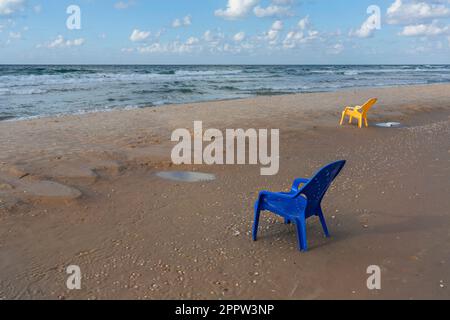 Plastikstühle am nassen Sandstrand des Ozeans, bat Yam, Israel Stockfoto