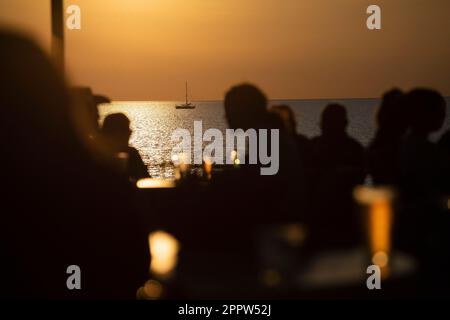 Die Leute, die bei Sonnenuntergang Bier auf der Terrasse am Meer tranken, waren abgeschirmt Stockfoto