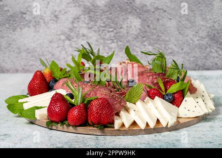 Antipasto-Set-Teller. Kaltgeräucherter Fleischteller. Antipasto mit Schinken, Prosciutto, Salami, Blauschimmelkäse, Mozzarella mit Blaubeeren und Erdbeeren Stockfoto