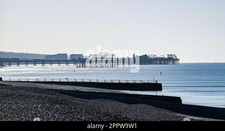 Brighton UK, 25. April 2023 - Ein Paddelboarder auf dem Meer vor Hove Beach mit Brightons zwei Piers im Hintergrund an einem sonnigen, aber kühlen Morgen entlang der Südküste : Credit Simon Dack / Alamy Live News Stockfoto