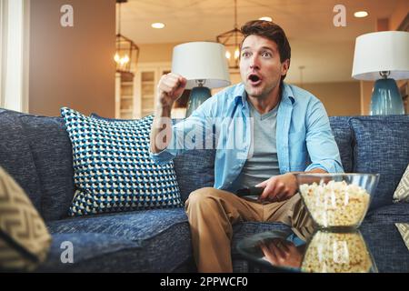 Echte Sportfans sehen sich das Spiel in Echtzeit an. Ein junger Mann, der ein aufregendes Sportspiel im fernsehen sieht. Stockfoto