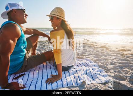 Lass uns einfach ewig in der Sonne verbringen. Ein glückliches Paar, das an einem sonnigen Tag am Strand saß. Stockfoto