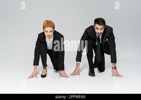 Stilvolle Geschäftsleute in schwarzen Hosenanzügen stehen in niedriger Startposition und schauen auf grauen Hintergrund auf die Kamera, Stockbild Stockfoto