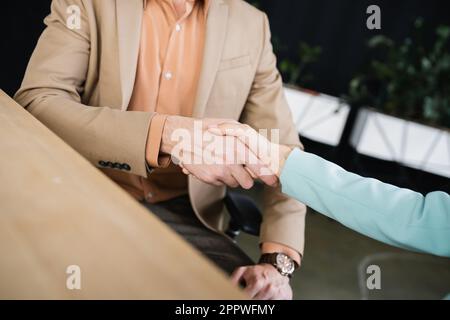 Teilansicht von Geschäftspartnern, die unscharfe Vordergründe im Büro mit den Händen schütteln, Aktienbild Stockfoto