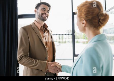 Erfolgreicher Geschäftsmann lächelt und schüttelt sich die Hand mit rothaariger Frau im Büro, Börsenbild Stockfoto