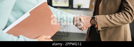 Teilansicht einer Frau mit Ordner, die einem Geschäftsmann im Büro die Hand schüttelt, Banner, Börsenbild Stockfoto
