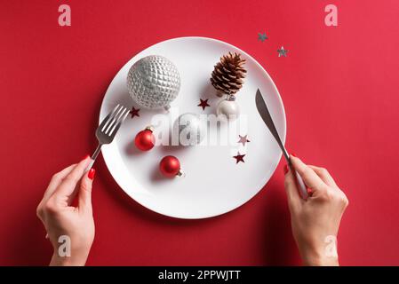 Schöne Tischdecke und weibliche Hände. Festliche silberne Kugeln und Kiefernzapfen auf weißem Schild auf rotem Hintergrund, flach liegend, Kopierbereich. Eati Stockfoto