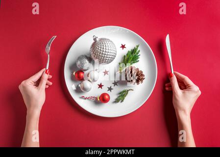 Schöne Tischdecke und weibliche Hände. Festliche silberne Kugeln und Kiefernzapfen auf weißem Schild auf rotem Hintergrund, flach liegend, Kopierbereich. Chri Stockfoto