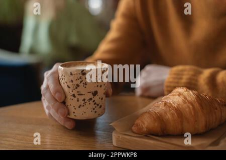 Nahaufnahme eines Mannes, der Kaffee trinkt und ein Croissant isst Stockfoto